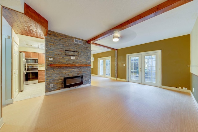 unfurnished living room with ceiling fan, french doors, beamed ceiling, light hardwood / wood-style floors, and a fireplace