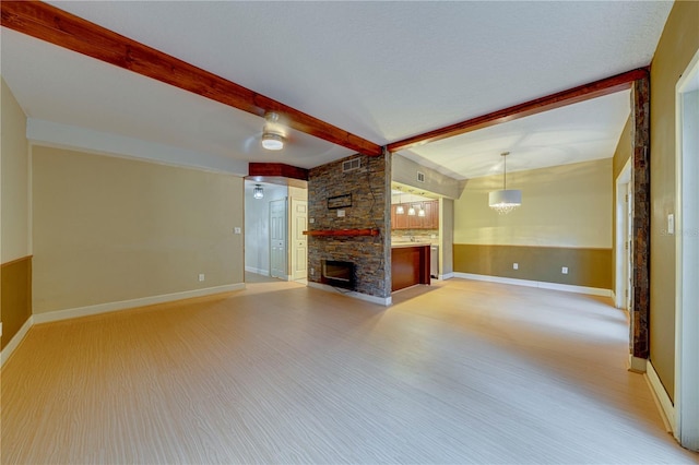 unfurnished living room featuring light hardwood / wood-style floors, a stone fireplace, beam ceiling, and a chandelier