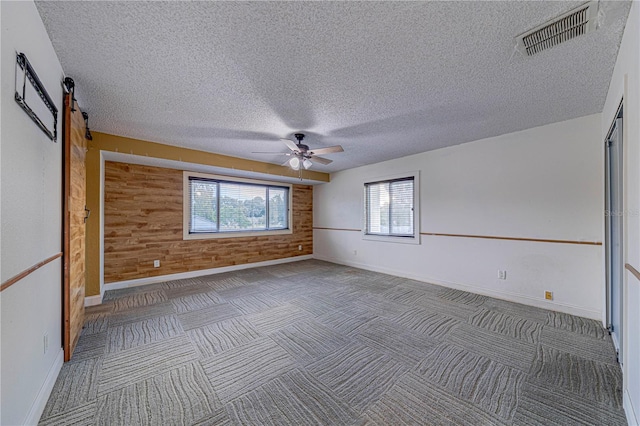 carpeted spare room with ceiling fan, a barn door, a textured ceiling, and wooden walls