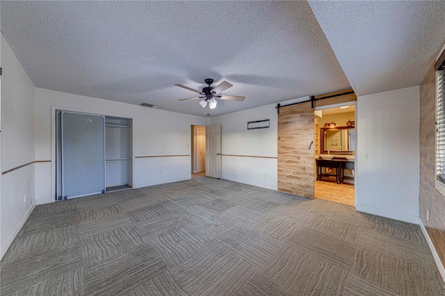 unfurnished bedroom featuring carpet flooring, ceiling fan, a barn door, a textured ceiling, and a closet