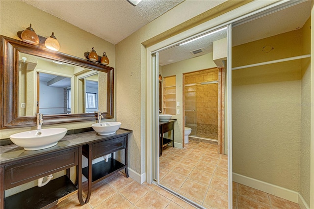 bathroom with walk in shower, vanity, a textured ceiling, tile patterned flooring, and toilet