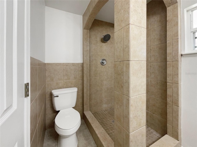 bathroom featuring a tile shower, toilet, and tile walls