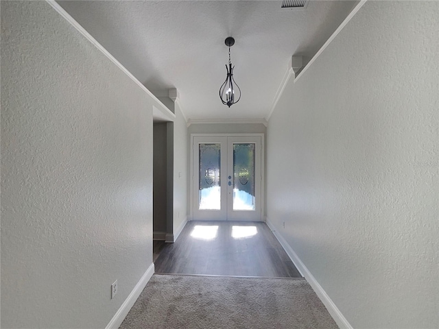 corridor with french doors, a textured ceiling, dark carpet, and ornamental molding