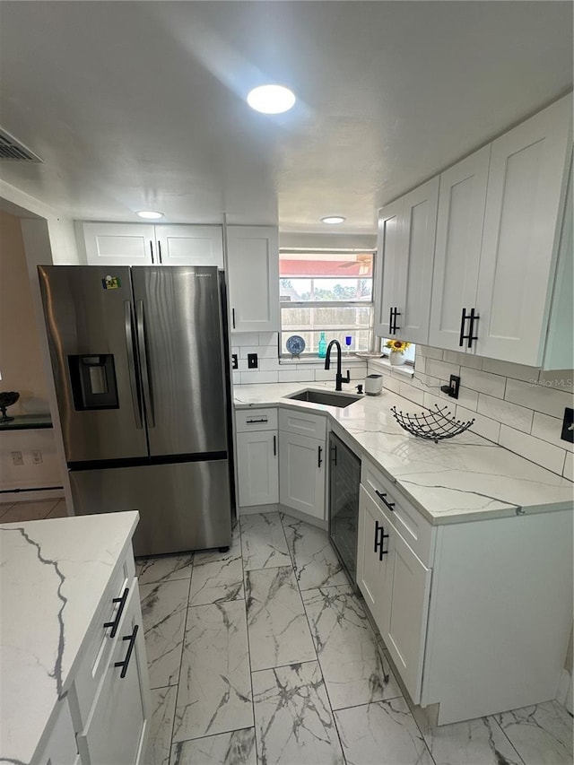 kitchen featuring white cabinets, light stone countertops, sink, and stainless steel fridge