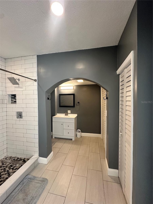 bathroom featuring a textured ceiling, vanity, and a tile shower