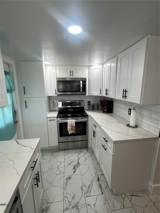 kitchen featuring tasteful backsplash, white cabinetry, light stone countertops, and appliances with stainless steel finishes