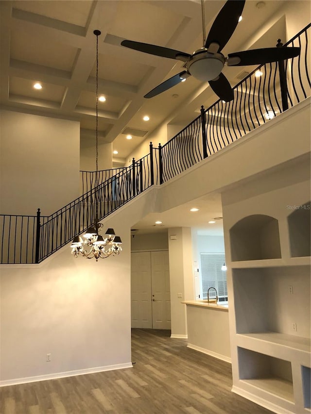 empty room with a high ceiling, coffered ceiling, ceiling fan with notable chandelier, hardwood / wood-style flooring, and beam ceiling