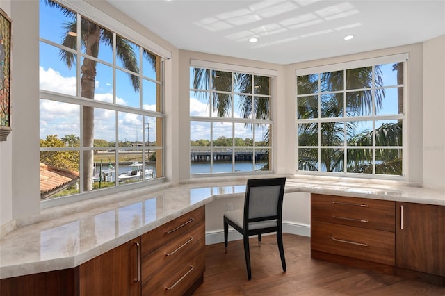 office area featuring plenty of natural light, dark wood-style floors, built in desk, and a water view