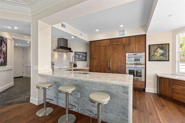 kitchen with a kitchen bar, modern cabinets, dark wood-style floors, stainless steel double oven, and brown cabinetry