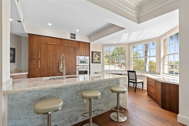 kitchen featuring light stone counters, brown cabinets, light wood-type flooring, and a sink