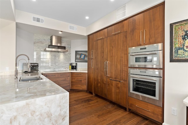 kitchen featuring visible vents, wall chimney range hood, brown cabinets, stainless steel double oven, and modern cabinets