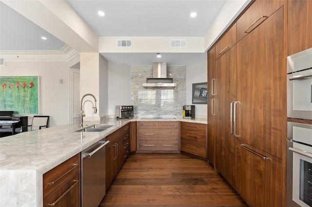 kitchen with visible vents, a peninsula, a sink, dishwasher, and wall chimney range hood