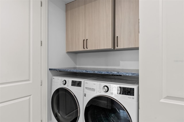 clothes washing area featuring cabinet space and washer and clothes dryer