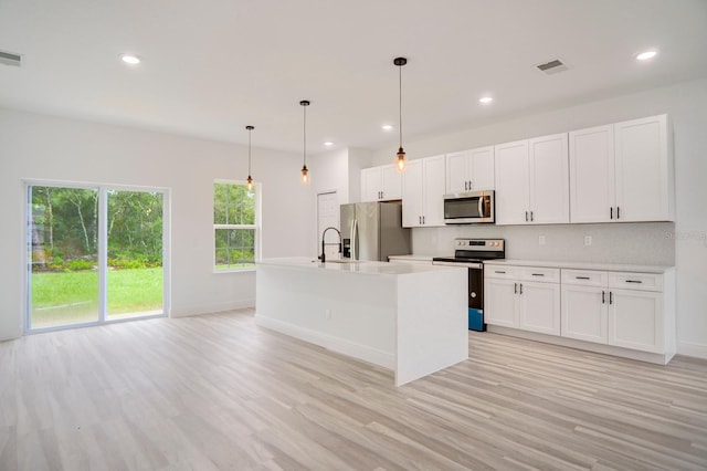 kitchen with hanging light fixtures, light wood-type flooring, an island with sink, white cabinetry, and stainless steel appliances