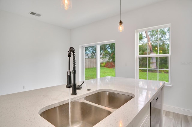 kitchen featuring decorative light fixtures, light stone counters, a healthy amount of sunlight, and sink