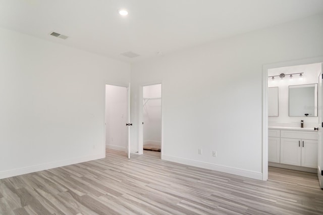 unfurnished bedroom featuring connected bathroom, a walk in closet, a closet, and light wood-type flooring