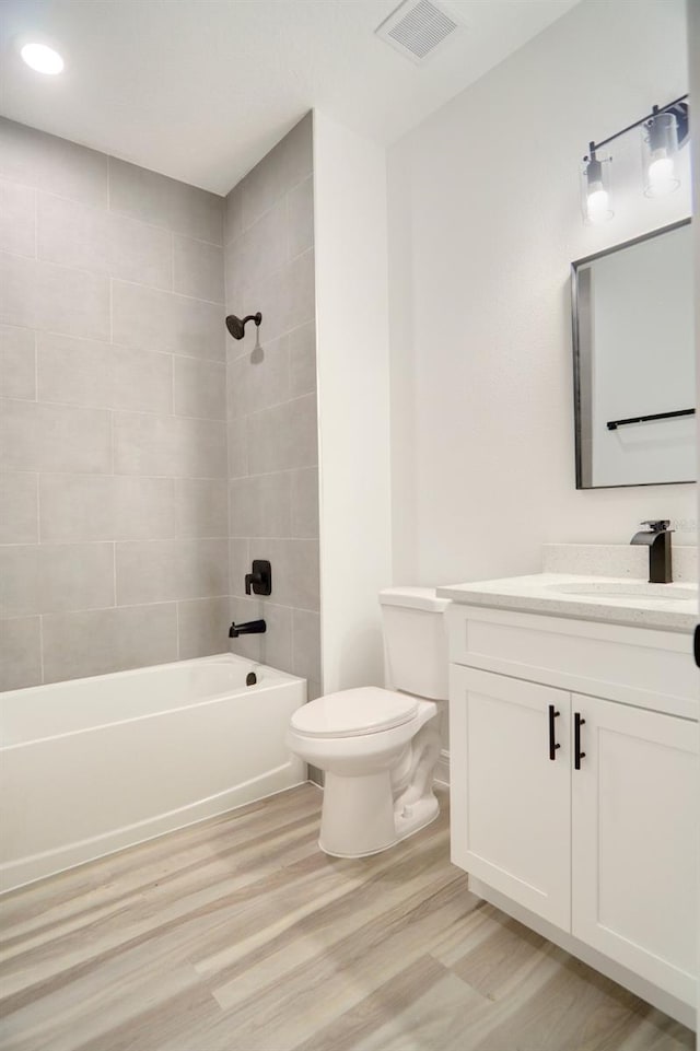 full bathroom featuring hardwood / wood-style floors, tiled shower / bath combo, toilet, and vanity