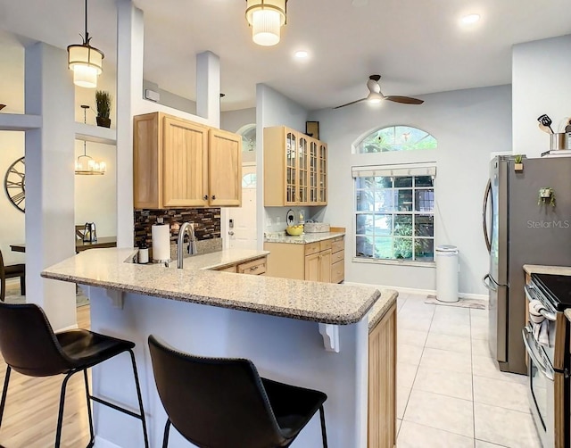 kitchen featuring kitchen peninsula, a kitchen breakfast bar, ceiling fan with notable chandelier, stainless steel appliances, and hanging light fixtures