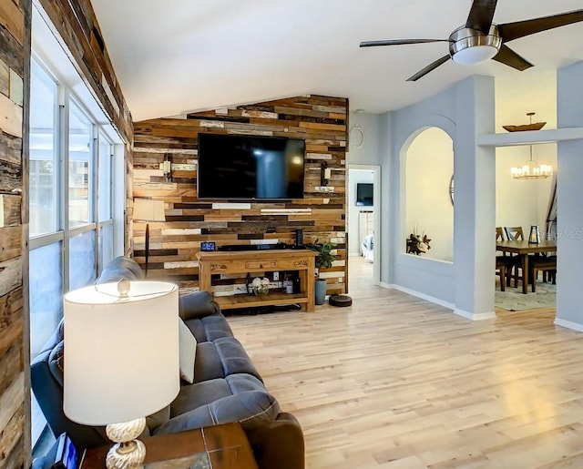 living room featuring vaulted ceiling, wood walls, ceiling fan with notable chandelier, and light wood-type flooring