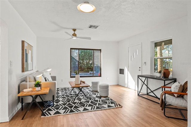 living room featuring ceiling fan, a textured ceiling, and light wood-type flooring