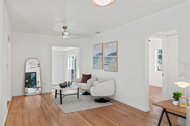 living room with ceiling fan, light hardwood / wood-style floors, and a textured ceiling