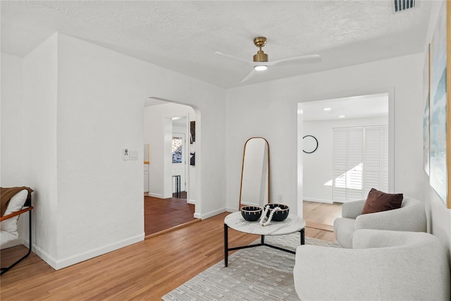 living area featuring hardwood / wood-style flooring, ceiling fan, and a textured ceiling