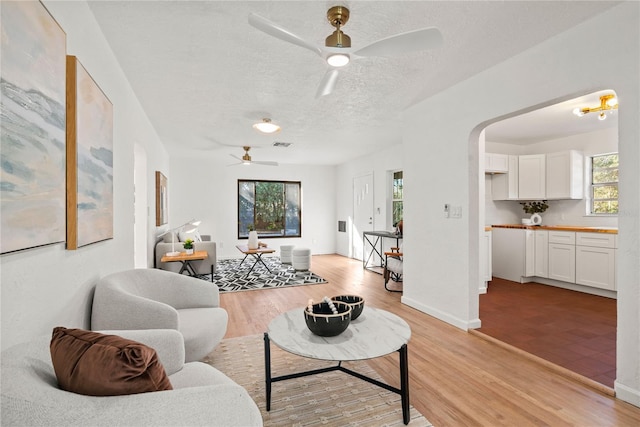 living room with a textured ceiling, ceiling fan, and light wood-type flooring