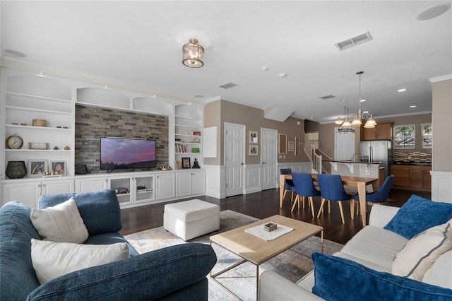 living room featuring built in shelves, crown molding, dark hardwood / wood-style flooring, and an inviting chandelier