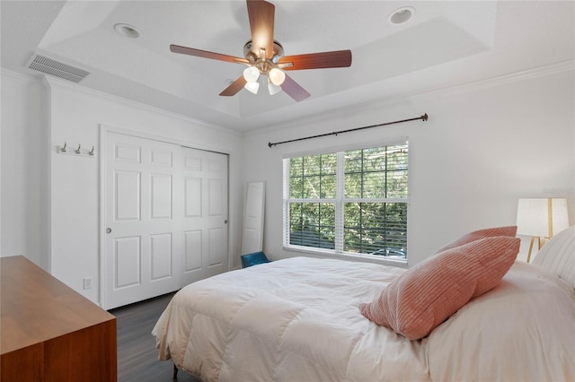 bedroom featuring a raised ceiling, dark hardwood / wood-style flooring, ceiling fan, and a closet