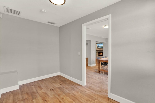 empty room with light wood-type flooring and a brick fireplace