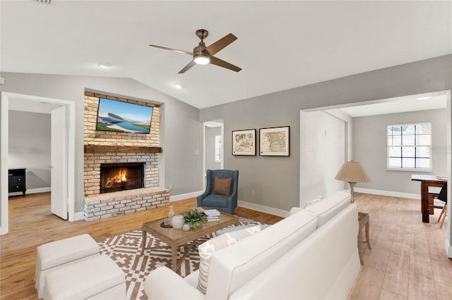 living room featuring ceiling fan, light hardwood / wood-style floors, a fireplace, and vaulted ceiling