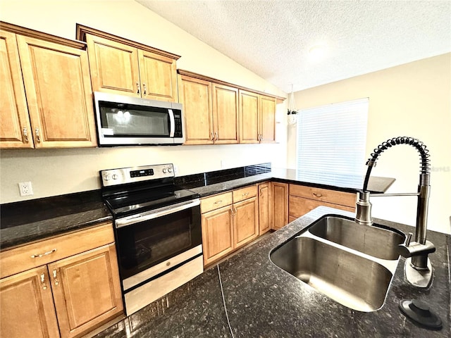 kitchen featuring sink, vaulted ceiling, a textured ceiling, decorative light fixtures, and stainless steel appliances