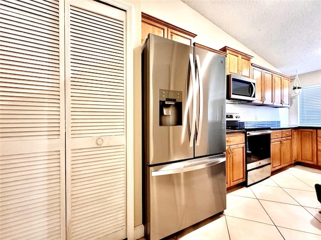 kitchen featuring hanging light fixtures, vaulted ceiling, light tile patterned floors, a textured ceiling, and appliances with stainless steel finishes