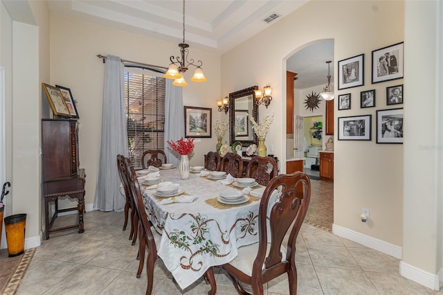 dining space with a raised ceiling, light tile patterned floors, and a chandelier