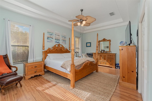 bedroom with ceiling fan, a tray ceiling, and light hardwood / wood-style flooring