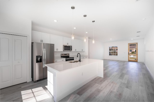 kitchen with a center island with sink, white cabinets, sink, hanging light fixtures, and stainless steel appliances