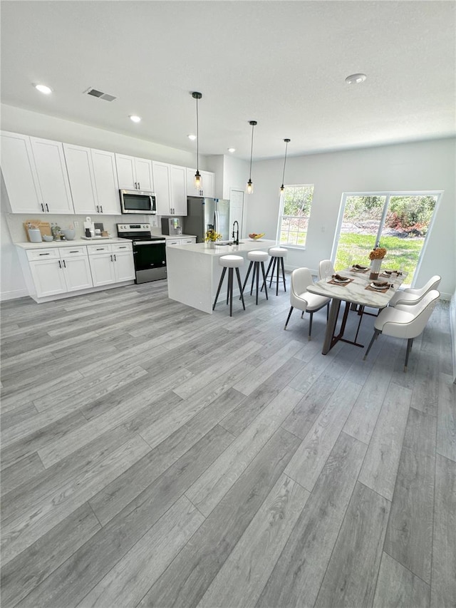 kitchen with appliances with stainless steel finishes, a kitchen island with sink, sink, pendant lighting, and white cabinetry