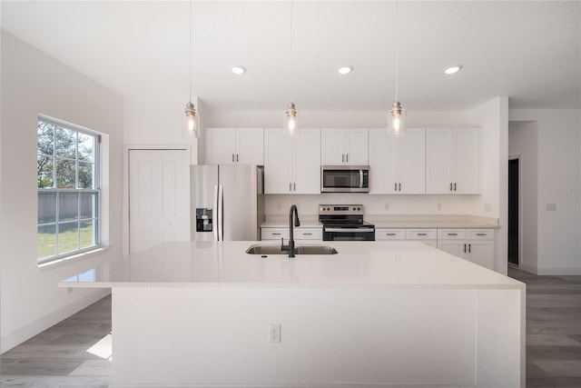 kitchen with hanging light fixtures, sink, stainless steel appliances, and a kitchen island with sink