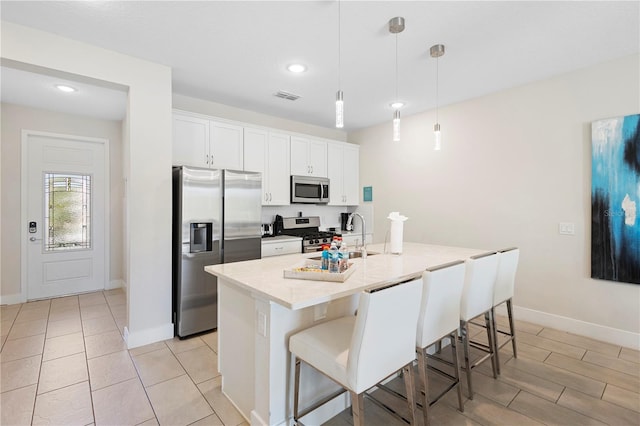 kitchen with stainless steel appliances, pendant lighting, a center island with sink, white cabinetry, and a breakfast bar area