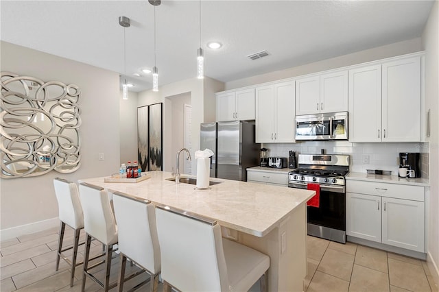 kitchen with a center island with sink, white cabinets, sink, hanging light fixtures, and appliances with stainless steel finishes