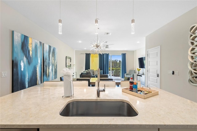 kitchen featuring light stone counters, an island with sink, pendant lighting, and an inviting chandelier