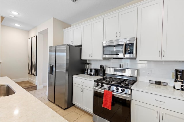 kitchen with white cabinetry, stainless steel appliances, light stone counters, backsplash, and light tile patterned floors