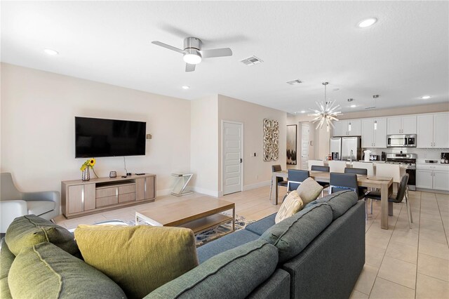 tiled living room with ceiling fan with notable chandelier