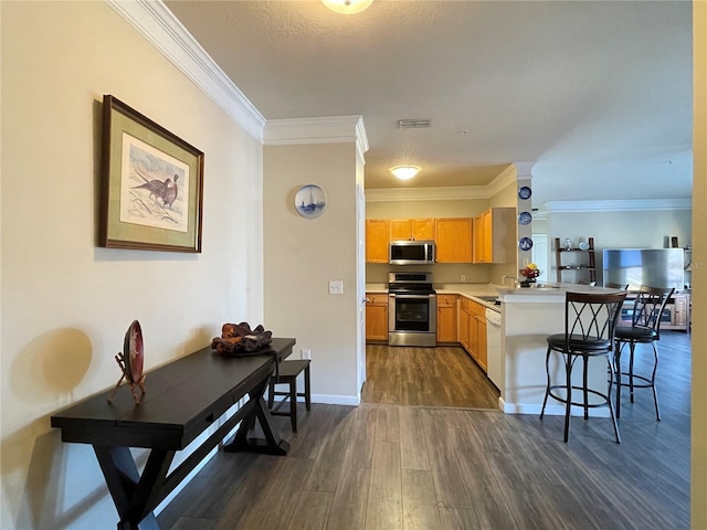 kitchen featuring stainless steel appliances, dark hardwood / wood-style flooring, kitchen peninsula, crown molding, and a kitchen bar