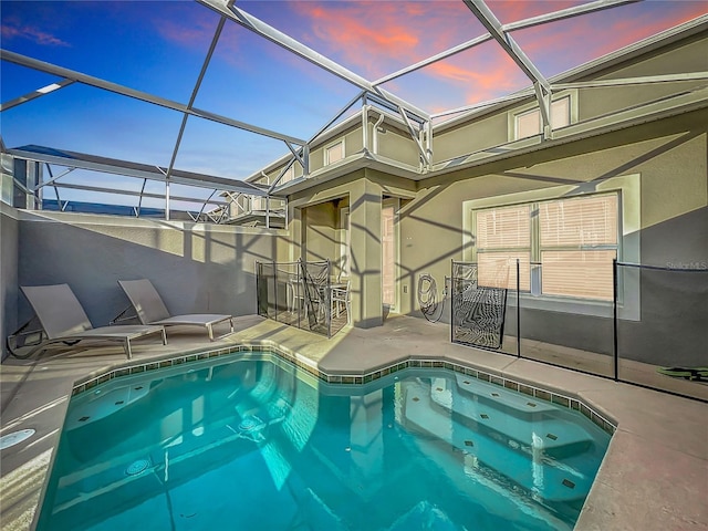 pool at dusk with glass enclosure and a patio