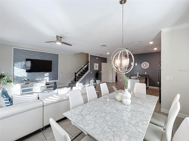 dining space featuring crown molding, sink, light tile patterned floors, and ceiling fan with notable chandelier