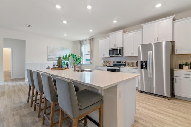 kitchen with appliances with stainless steel finishes, a breakfast bar, white cabinets, a kitchen island with sink, and light hardwood / wood-style floors