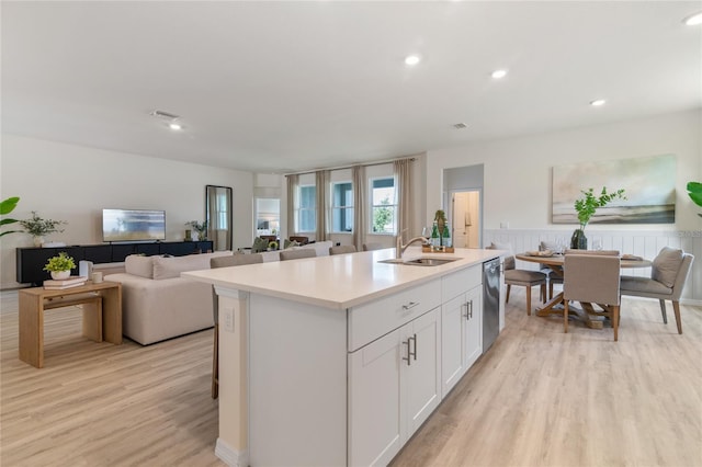 kitchen featuring sink, white cabinets, a kitchen island with sink, stainless steel dishwasher, and light hardwood / wood-style floors