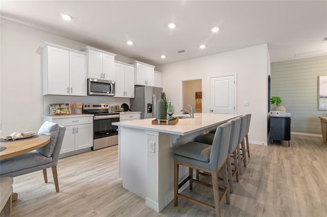 kitchen with sink, a breakfast bar, appliances with stainless steel finishes, a kitchen island with sink, and white cabinetry