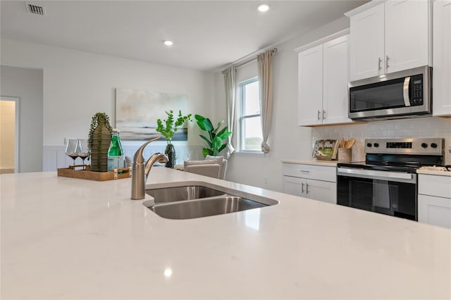 kitchen with stainless steel appliances, sink, white cabinets, and backsplash